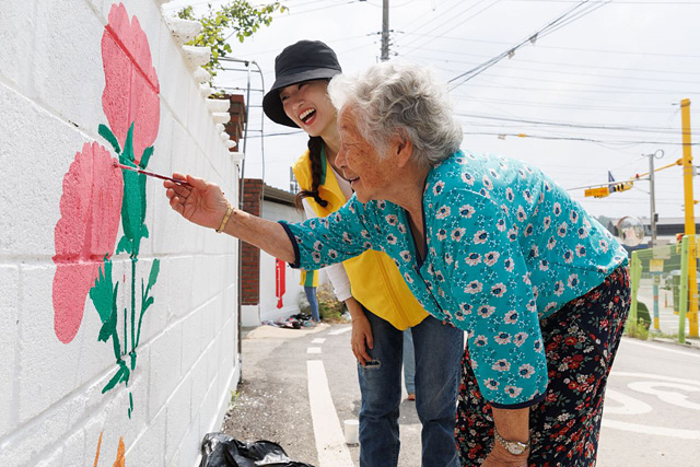 '담벼락 이야기' 봉사활동. 봉사자가 주민과 함께 벽화를 그리고 있다.jpg
